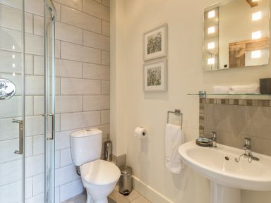 A bathroom with a toilet sink mirror glass shower and framed pictures on the wall at Sawmill Cottage Belford near Bamburgh