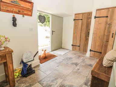 An entrance hall with a wooden bench a cushion two wooden doors a green door a coat rack a table with flowers tennis rackets and tennis balls at Sawmill Cottage in Belford near Bamburgh
