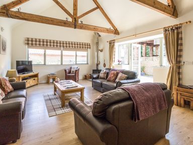A living room with wooden beams leather sofas a coffee table and a television at Sawmill Cottage Belford near Bamburgh