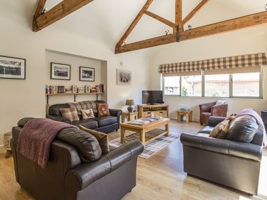 A living room with wooden beams leather sofas armchair and a wooden coffee table at Sawmill Cottage in Belford near Bamburgh
