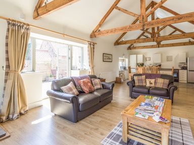 A living room with two leather sofas a wooden coffee table and exposed wooden beams at Sawmill Cottage in Belford near Bamburgh