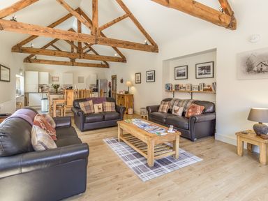 A living room with wooden beams on the ceiling leather sofas a wooden coffee table and an open kitchen with dining table at Sawmill Cottage Belford near Bamburgh