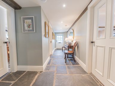 A hallway with stone tile flooring wooden chairs a console table with lamps and a round mirror at Prospect House in Ambleside