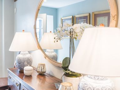A wooden sideboard with two table lamps a potted orchid and decorative items in front of a round mirror at Prospect House in Ambleside