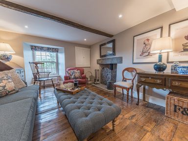 A living room with wooden floor a gray sofa a red armchair a wooden chair a fireplace and a wooden table with a lamp at Prospect House in Ambleside