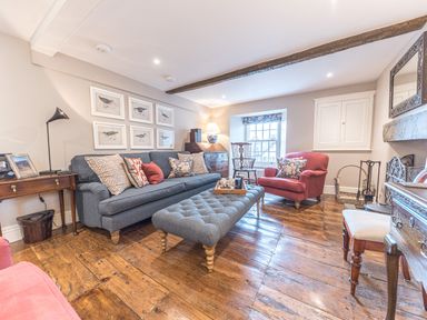 A living room with a blue sofa and ottoman red armchairs wooden flooring and framed bird pictures at Prospect House in Ambleside