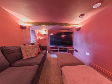 A small media room with a sectional sofa and ottomans facing a large flat screen TV at Prospect House in Ambleside