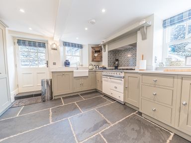 A kitchen with grey cabinets a white stove blue and white tile backsplash and slate flooring at Prospect House in Ambleside