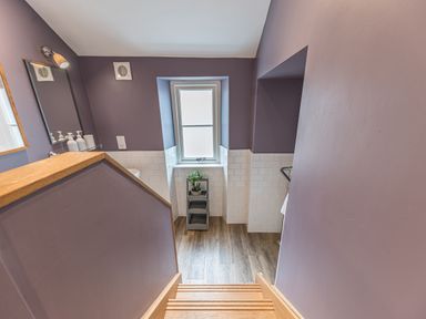 A stairway leading down to a bathroom with purple walls a window and a small plant on a shelving unit at Prospect House in Ambleside