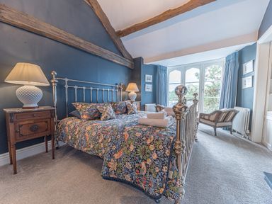 A bedroom with a metal bed frame floral bedspread bedside tables lamps armchairs and large windows at Prospect House in Ambleside