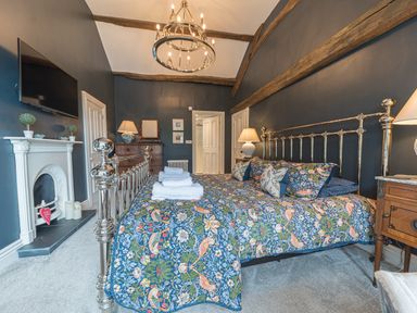 A bedroom with a metal bed frame and floral bedding dark walls wooden beams and a white fireplace at Prospect House in Ambleside