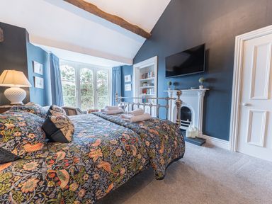 A bedroom with a patterned bedspread a lamp a TV on the wall and a fireplace at Prospect House in Ambleside