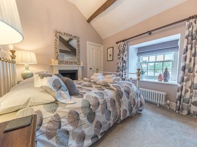 A bedroom with a bed with patterned bedding beside a window with curtains and a radiator at Prospect House in Ambleside