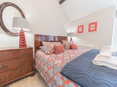 A bedroom with a bed with patterned bedding and pillows next to a wooden dresser with a lamp and a round mirror at Prospect House Ambleside