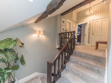 A carpeted staircase with wooden railing leading to a hallway with doors and wall lights at Prospect House in Ambleside