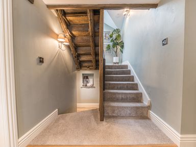 A carpeted staircase with wooden beams a potted plant on the landing and wall lights at Prospect House in Ambleside