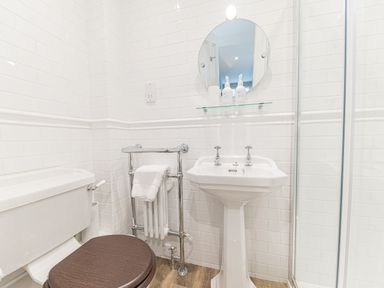 A bathroom with a toilet a pedestal sink a round mirror and a glass shower door at Prospect House in Ambleside