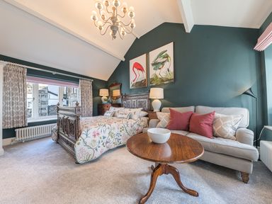 A bedroom with a wooden bed and floral bedspread a beige sofa with red and gray pillows and a round wooden coffee table in Prospect Cottage Loft Ambleside