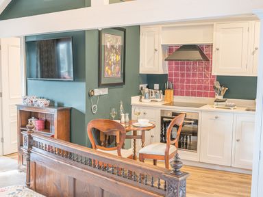 A kitchen with white cabinets a red tile backsplash a wooden table with two chairs and a TV on a green wall at Prospect Cottage Loft in Ambleside