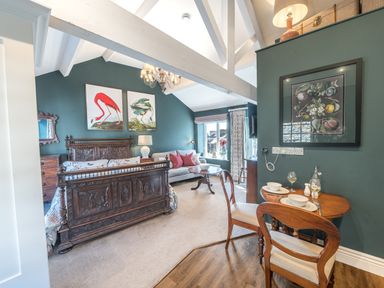 A bedroom with a wooden carved bed sofa small dining table with two chairs and bird pictures on green walls at Prospect Cottage Loft in Ambleside