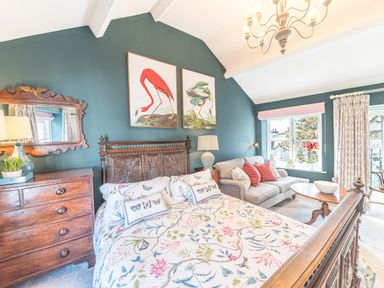 A bedroom with a carved wooden bed and floral bedding next to a wooden chest of drawers a beige sofa and a wooden coffee table by a window at Prospect Cottage Loft in Ambleside