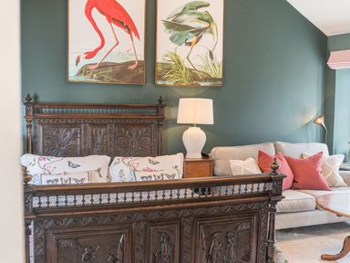 A bedroom with a carved wooden bed frame, floral bedding, a bedside table with a lamp, and a sofa with cushions at Prospect Cottage Loft in Ambleside