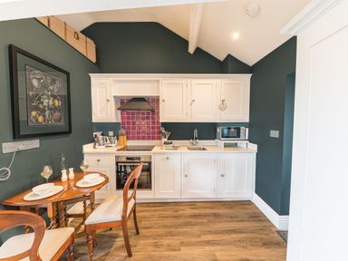 A kitchen with white cabinets wooden floor a small dining table with two chairs and kitchen appliances at Prospect Cottage Loft in Ambleside
