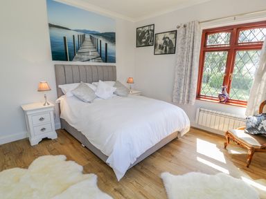 A bedroom with a bed lamps bedside tables a window with curtains and wooden flooring at Berwyn in Talybont