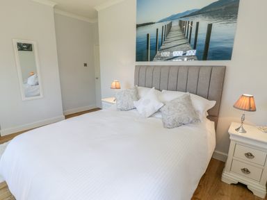 A bedroom with a bed with pillows two bedside tables with lamps a wall mirror and a large photo of a pier at Berwyn in Talybont