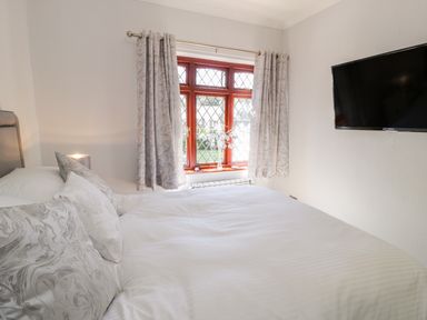 A bedroom with a bed, patterned pillows, a window with curtains, and a wall-mounted television at Berwyn in Talybont
