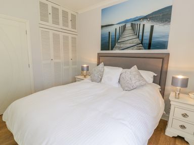 A bedroom with a double bed white bedding two nightstands lamps and a wall photo of a pier at Berwyn in Talybont