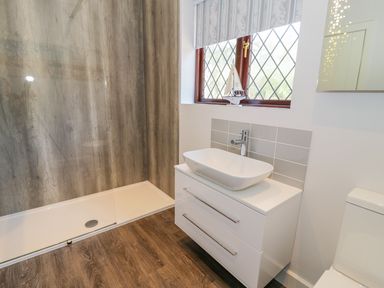 A bathroom with a walk-in shower a white sink on a cabinet and a window at Berwyn in Talybont