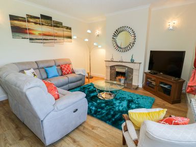 A living room with sofas a glass coffee table a fireplace a television and a multi panel sunset painting at Berwyn in Talybont