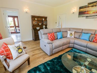 A living room with a grey sectional sofa with colorful cushions a wooden armchair with cushions a glass coffee table and a wooden cabinet at Berwyn in Talybont