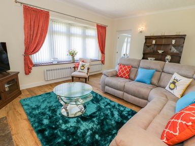 A living room with a glass coffee table and a teal rug by a grey sofa with colorful pillows at Berwyn in Talybont