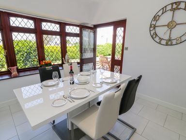 A dining area with a white table set with plates and glasses near windows and a door leading outside at Berwyn in Talybont