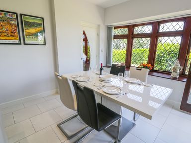 A dining area with a white dining table set with plates and wine glasses black and white chairs and large windows at Berwyn in Talybont