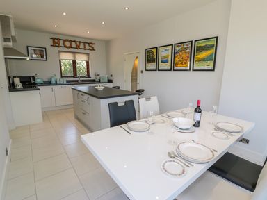 A dining table set with plates and wine bottle next to a kitchen with a central island and framed pictures on the wall at Berwyn in Talybont