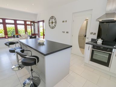 A kitchen with an island and black bar stools a dining table near windows and a stove with an oven at Berwyn in Talybont