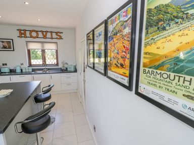 A kitchen area with white cabinets black countertops and two black bar stools with framed travel posters on the wall at Berwyn in Talybont