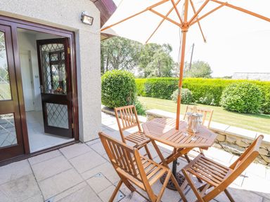 An outdoor patio with a wooden table and chairs under a large umbrella next to a garden at Berwyn in Talybont