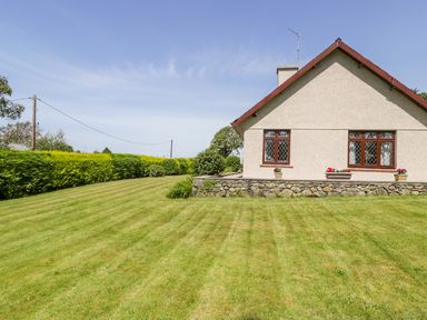 A side view of a house with a lawn and hedges at Berwyn in Talybont