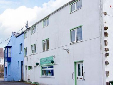 A white building with green trim and a sign reading Ocean Glade next to a blue building at The Old Brewery in Saundersfoot