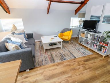 A living room with a grey sofa and yellow armchair next to a white coffee table and shelves with a TV at The Old Brewery in Saundersfoot