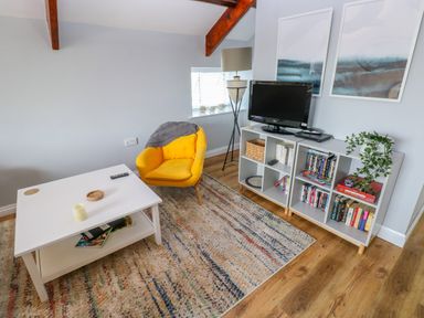 A living room with a yellow chair a white coffee table a television on a white shelving unit and a floor lamp at The Old Brewery in Saundersfoot