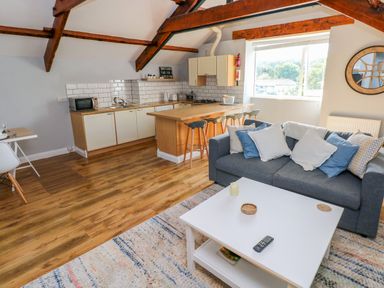 An open plan living room and kitchen with wooden beams a grey sofa and a wooden kitchen island at The Old Brewery in Saundersfoot