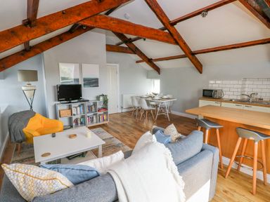 An open living space with a gray sofa yellow armchair white dining table kitchen counter and exposed wooden beams at The Old Brewery in Saundersfoot