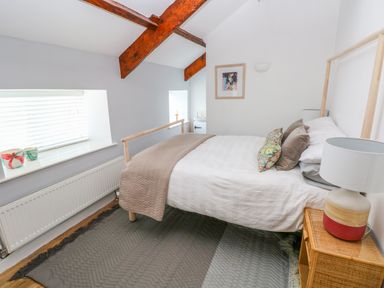 A bedroom with a bed a nightstand lamp and exposed wood beams at The Old Brewery in Saundersfoot