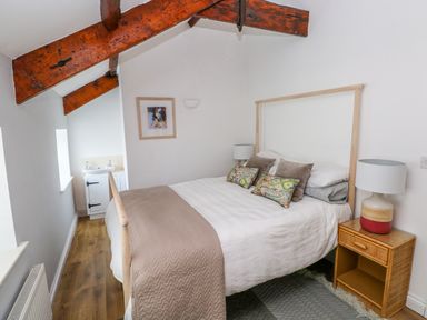 A bedroom with a bed cushions bedside table lamp and wooden beams at The Old Brewery in Saundersfoot
