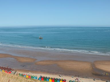 A beach with colorful beach huts along a promenade and a ship sailing on the ocean near Whitby